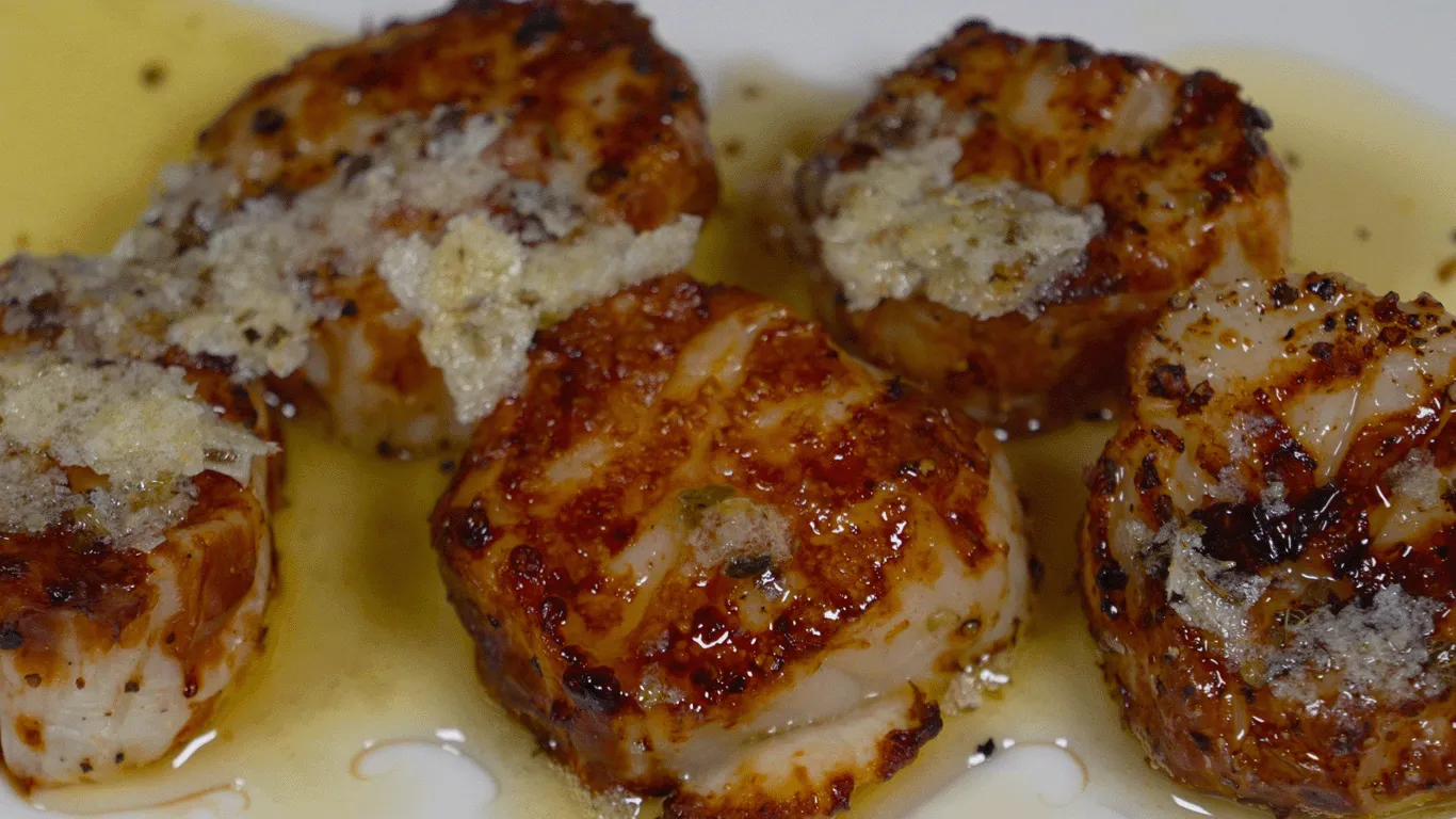 Cooked Sea Scallops on a plate covered in a butter sauce